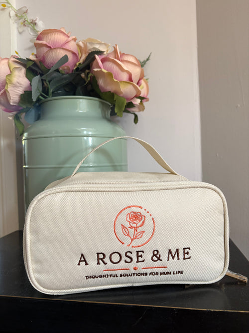 White pouch with 'A Rose & Me' branding next to a vase with flowers on a light surface.
